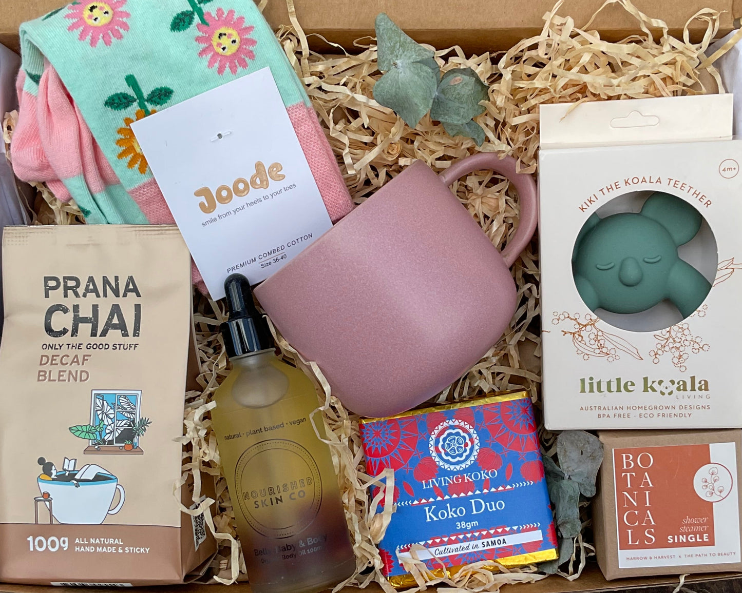 Gift box with various items including a pink mug, soap, and tea packaging on a rustic surface.
