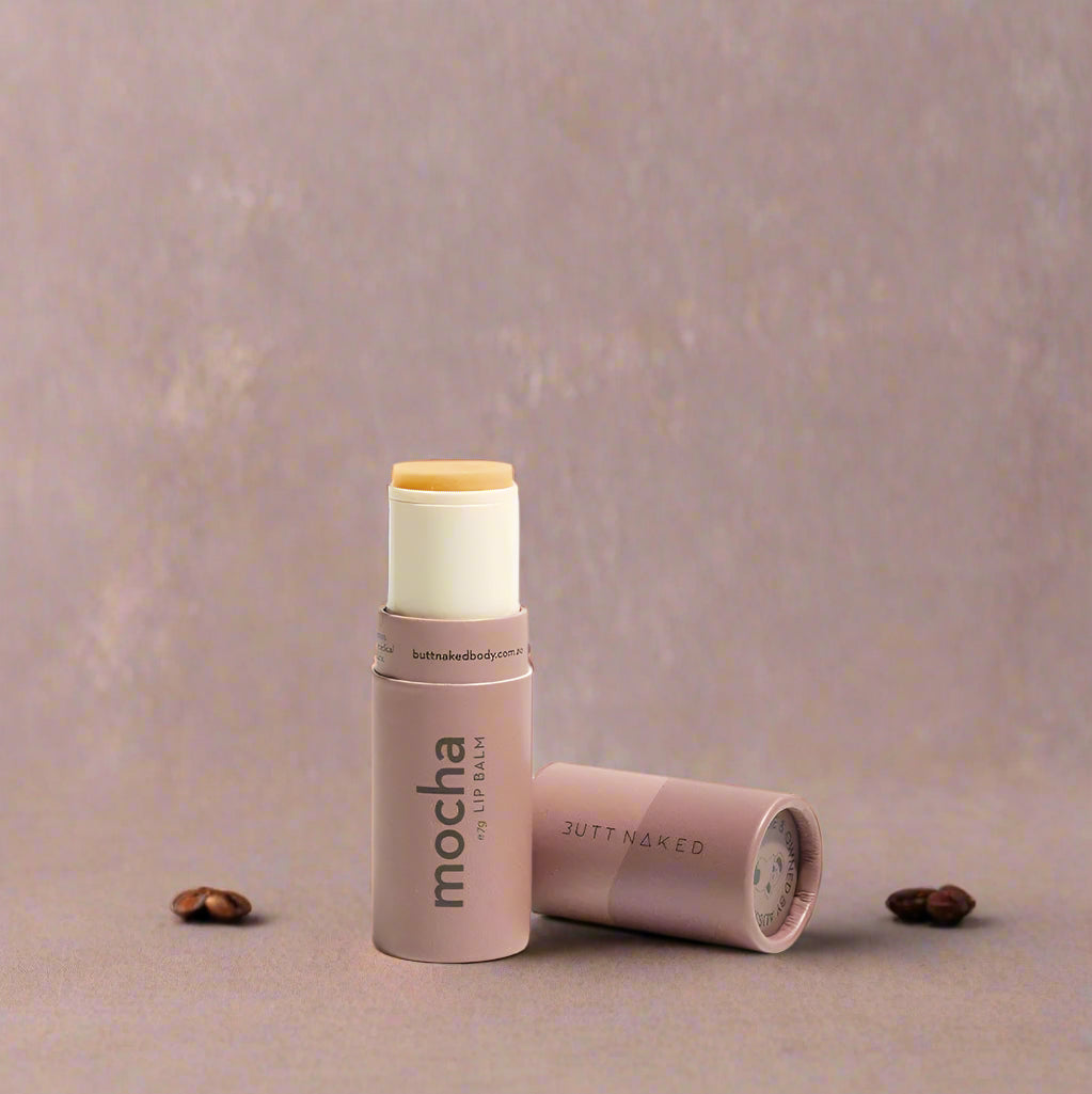 A tube of mocha lip balm lying next to its open cap on a light background.