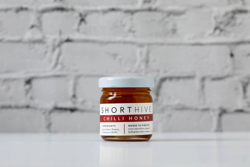 Jar of Shorthive Chilli Honey on a white surface with a brick wall background