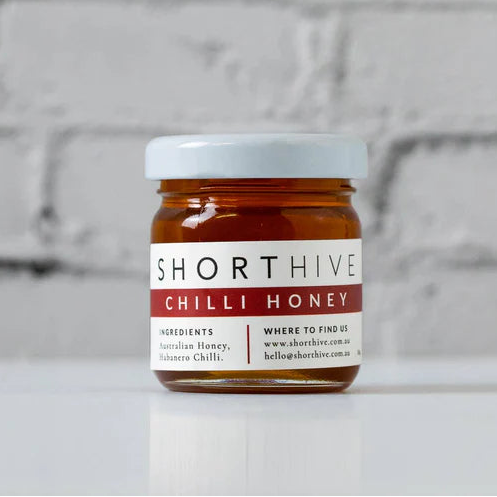 Jar of Shorthive Chilli Honey on a white surface with a brick wall background