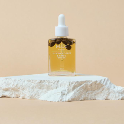 This is an image of a glass bottle of coffee body oil on a white rock