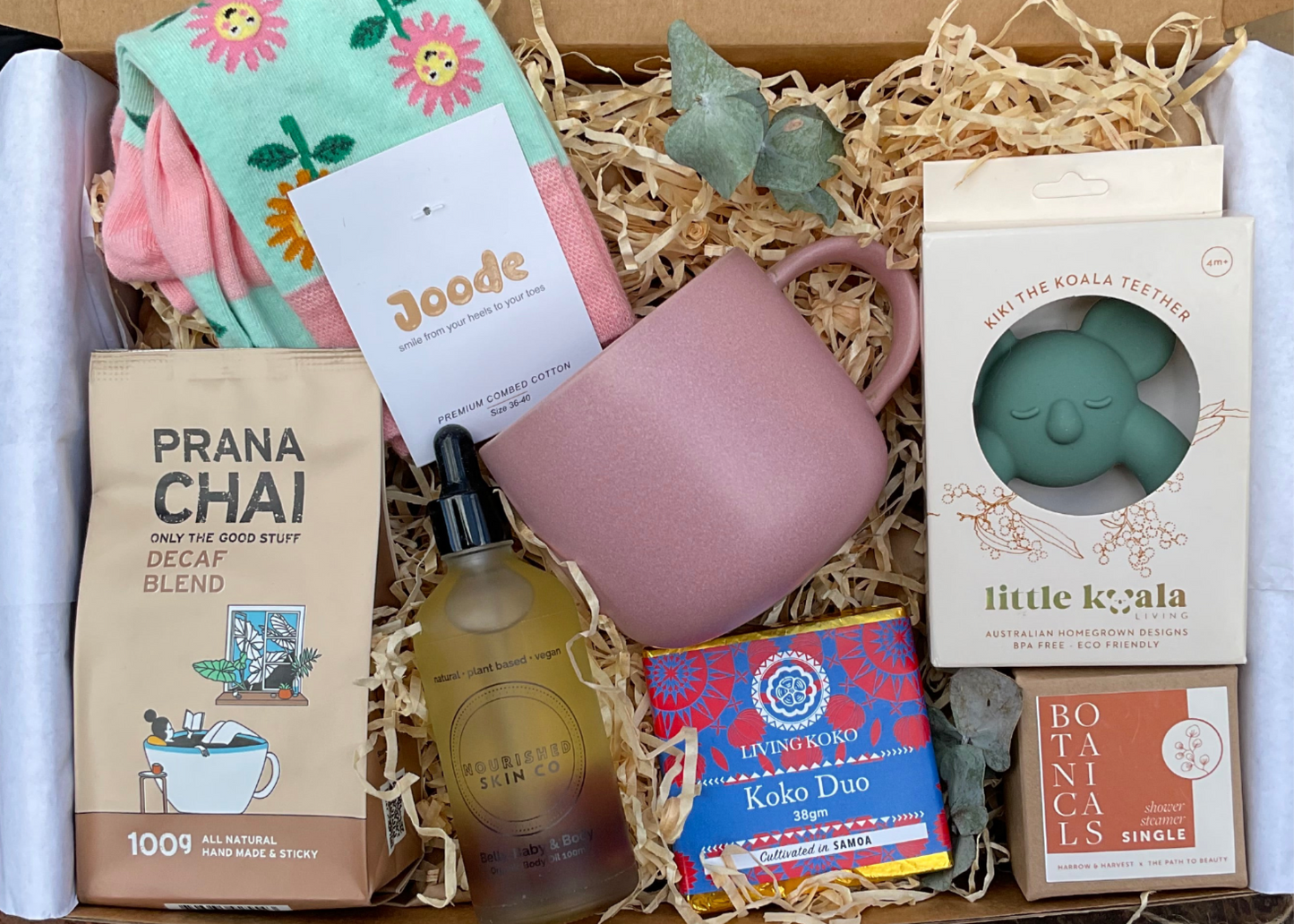 Gift box with various items including a mug, tea, and a plant, with a visible brand card.