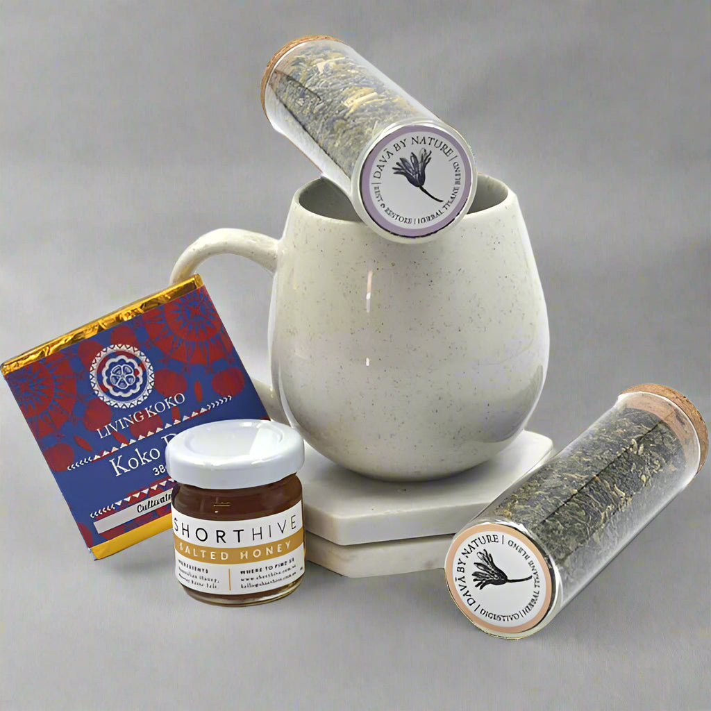 A collection of tea-related products including a ceramic mug, test tube teas, salted honey, and cacao powder, all arranged on a table.