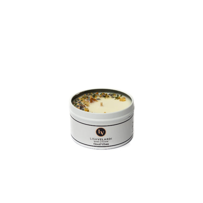 A white candle with botanicals embedded in it, presented in a metal tin with a label.