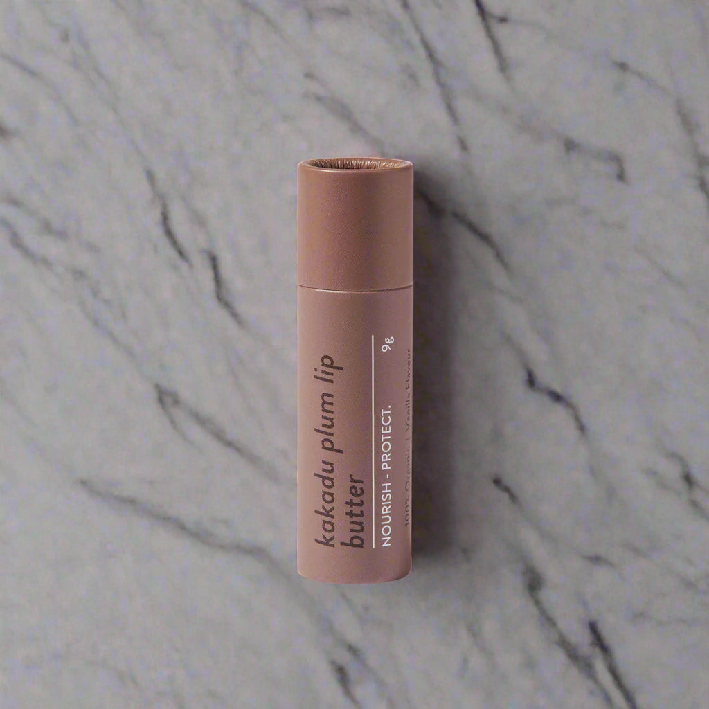 A stick of MIOD Kakadu Plum Lip Butter in a brown container with product details printed on it, placed against a white background.