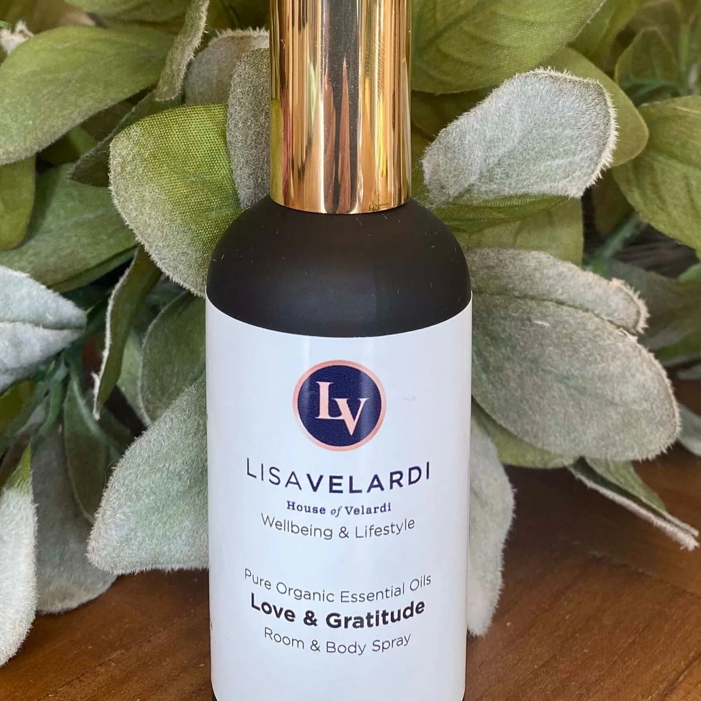 A 100ml glass spray bottle of 'Love and Gratitude' room and body mist by House of Velardi, with a label and a gold-colored cap.