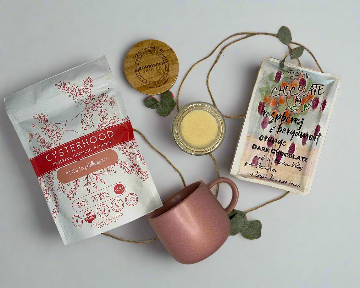 Pink mug, packets of tea, and a small jar on a white surface with decorative elements.