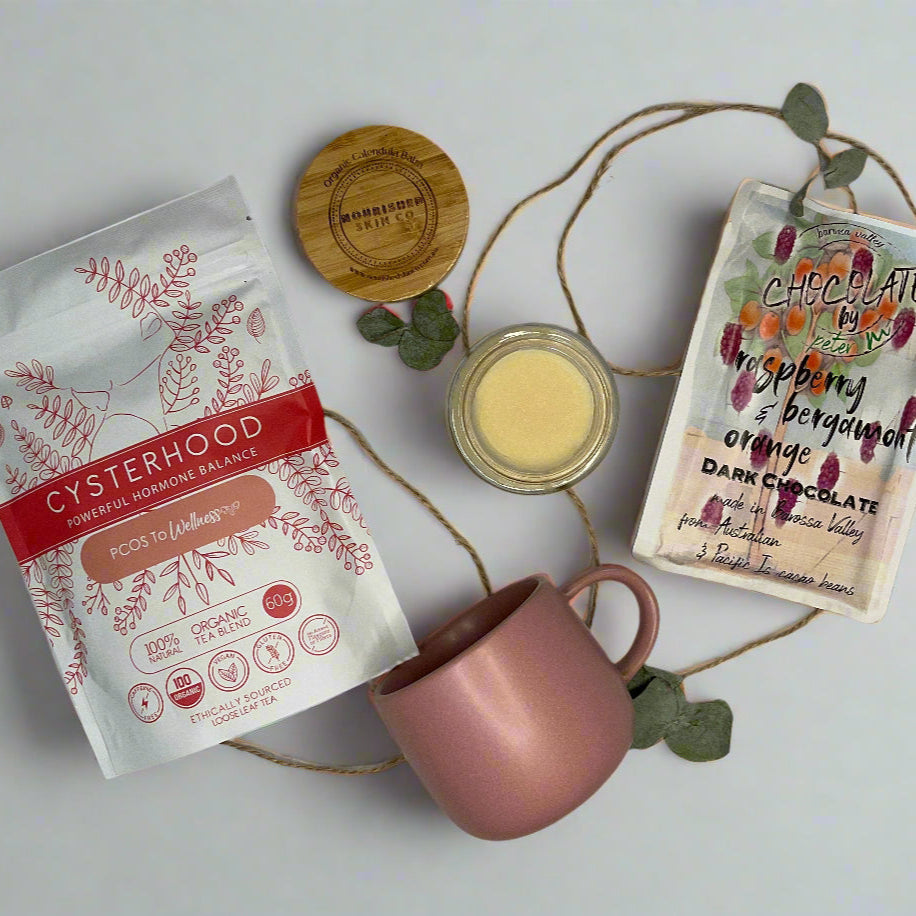 Pink mug, packets of tea, and a small jar on a white surface with decorative elements.