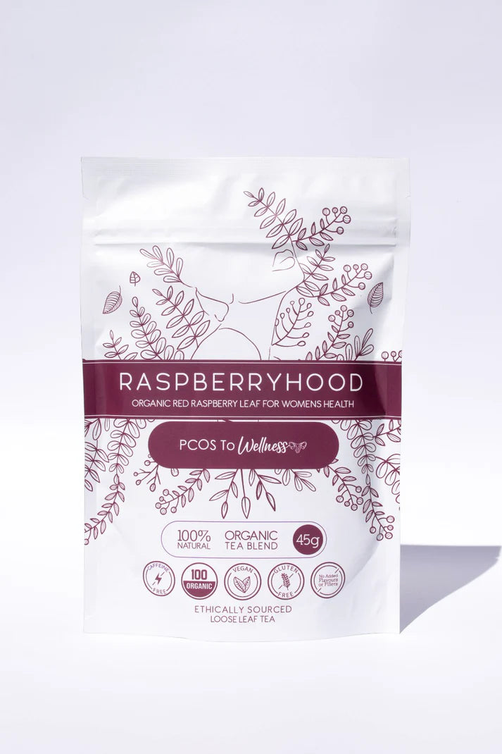 A packaged tea product, labeled 'Raspberryhood' with a subtitle 'PCOS to Wellness' on a white background. The packaging is predominantly white with purple and green botanical designs and text.