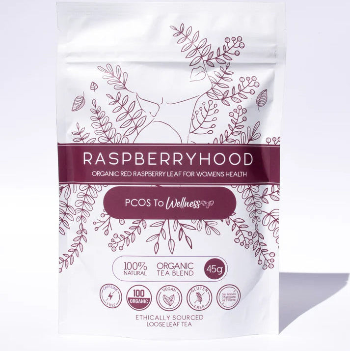 A packaged tea product, labeled 'Raspberryhood' with a subtitle 'PCOS to Wellness' on a white background. The packaging is predominantly white with purple and green botanical designs and text.