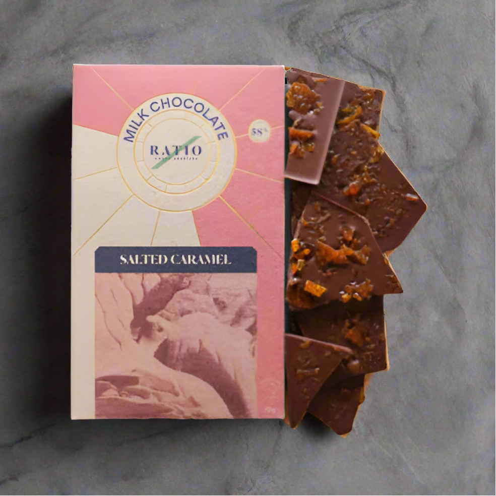 Milk chocolate bar with salted caramel pieces next to its packaging on a white background