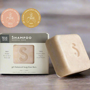 A solid shampoo bar alongside its packaging box, with badges indicating awards won. The packaging is labeled 'Shampoo for Normal Hair' and mentions organic and fair-trade ingredients.