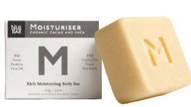 A solid moisturizer bar with the letter 'M' embossed on it, next to its packaging which reads 'NueBar Moisturiser Organic Cacao and Shea'. The bar is beige and the packaging is white with black text.