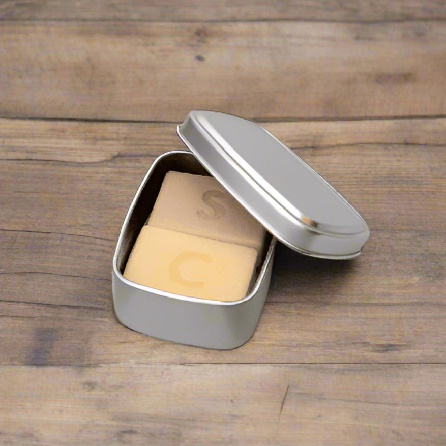 A small open tin container with a solid block of coconut oil inside, labeled with the letter 'S'.