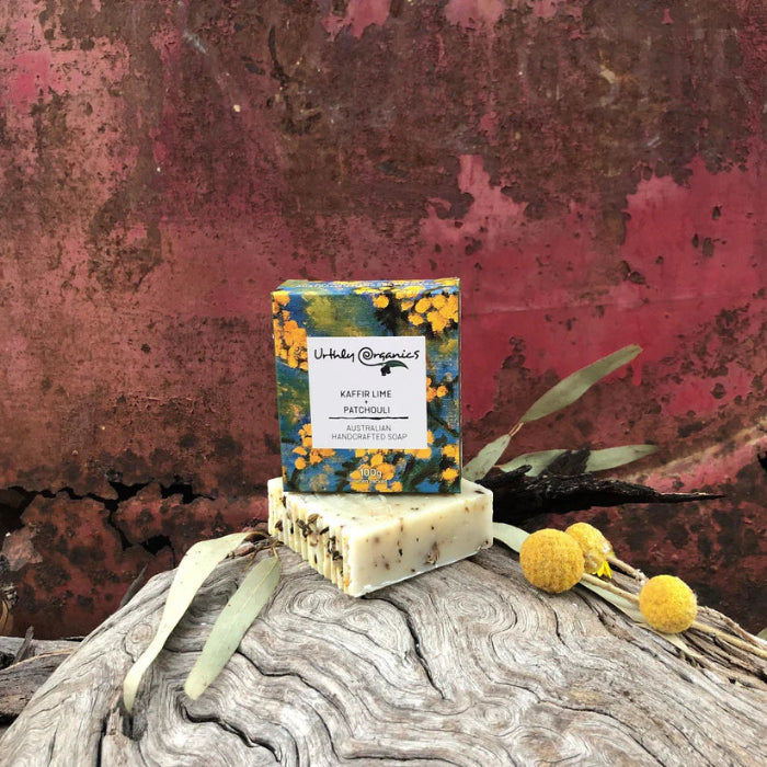 A bar of soap with natural patterns on its surface, placed on a wooden surface with a colorful floral packaging behind it.