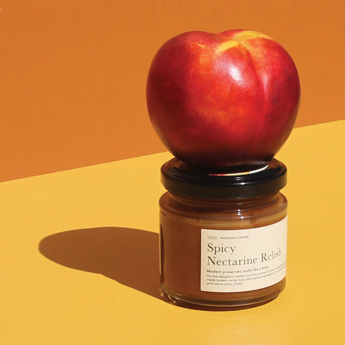 A jar of Spicy Nectarine Relish with a fresh nectarine placed on top of it, set against a split orange and yellow background.