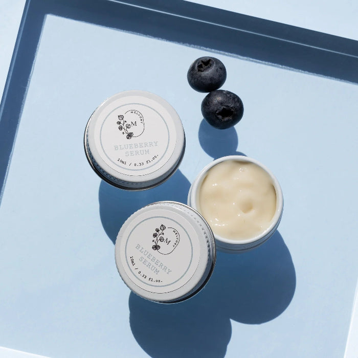 this is an image of blueberry serum in 2 little jars and 2 blueberries on a blue tray
