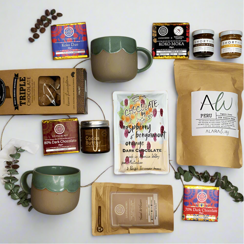 A collection of luxury coffee and cacao treats including various chocolates, coffee beans, cookies, mugs, and honey, displayed on a white surface with decorative foliage.