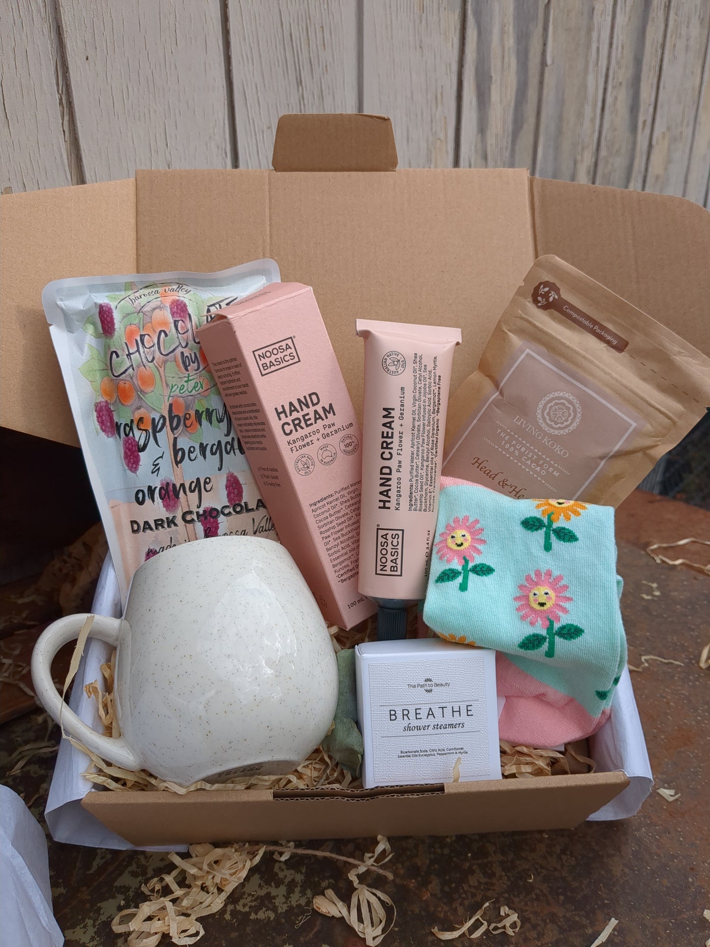 Assorted items including a mug, soap, and books in a cardboard box on a wooden surface.