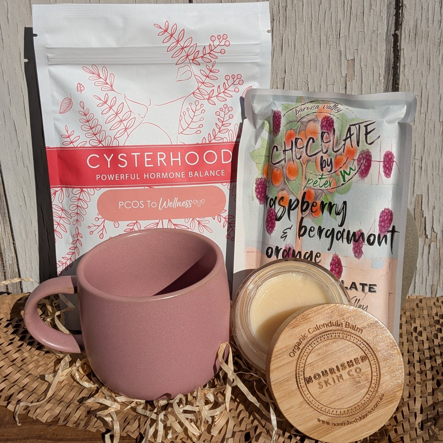 Pink mug with a package of 'Cysterhood' and a chocolate bar on a wooden surface.