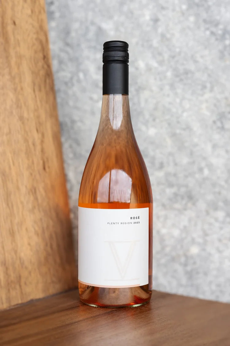 Bottle of rose wine with a white label on a wooden surface.
