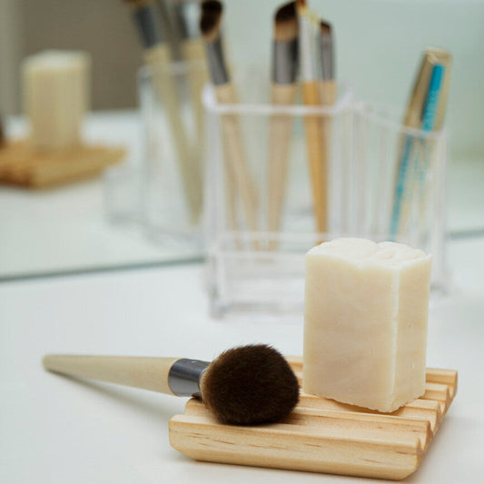 Makeup brushes in holders with a bar of soap on a wooden block on a white surface.