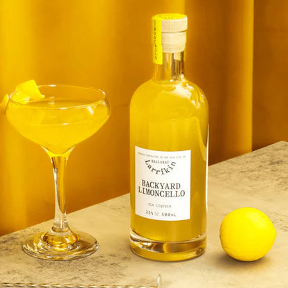 Bottle of Backyard Limoncello with a glass of limoncello and lemon on a yellow background