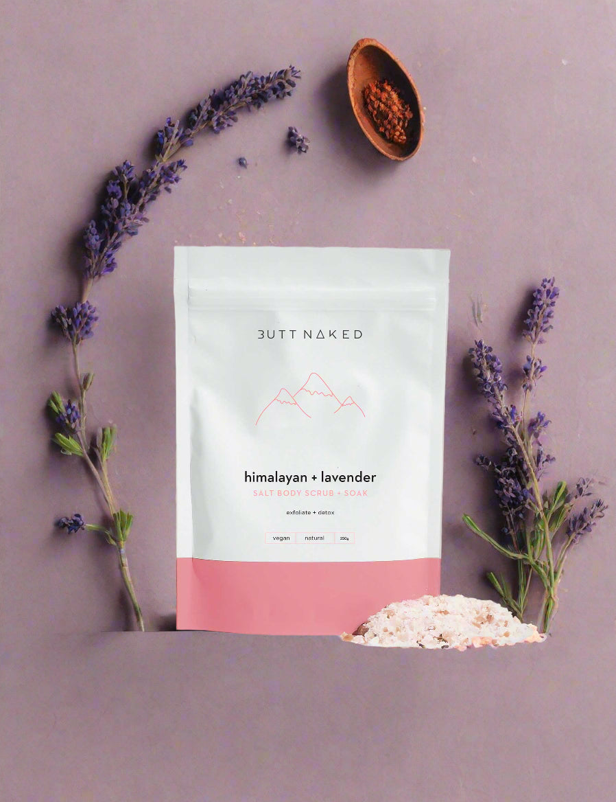 A package of Butt Naked Body Himalayan & Lavender scrub and soak with a small pile of pinkish bath salts in front of it.