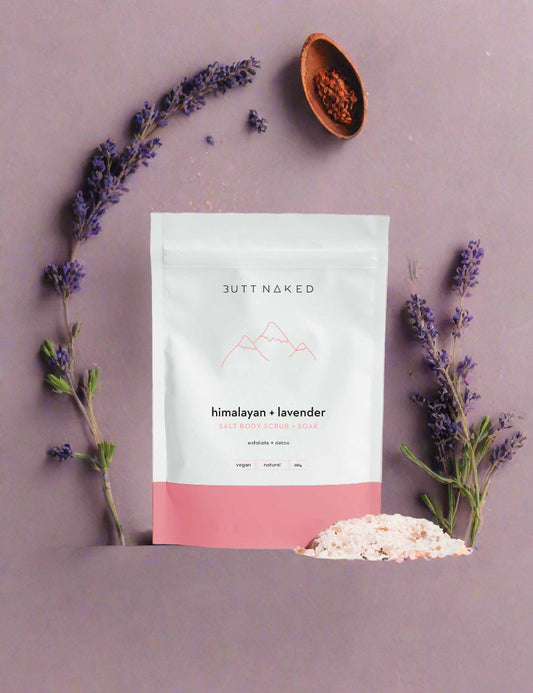 A package of Butt Naked Body Himalayan & Lavender scrub and soak with a small pile of pinkish bath salts in front of it.