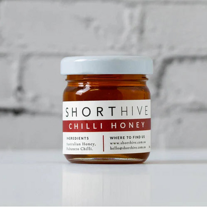 Jar of Shorthive Chilli Honey on a white surface with a brick wall background