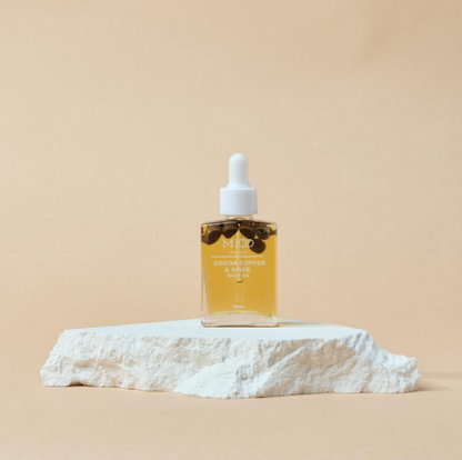 This is an image of a glass bottle of coffee body oil on a white rock