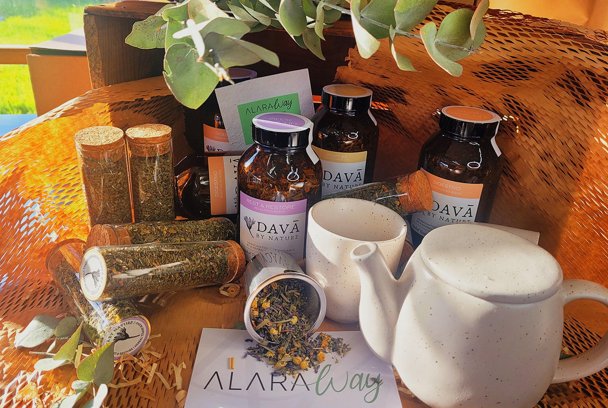 Herbal products and teapots on a table with 'Alara Way' branding.