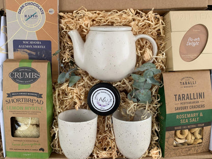 Gift set with ceramic teapot, cups, and snacks in a box