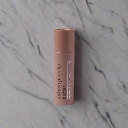 A stick of MIOD Kakadu Plum Lip Butter in a brown container with product details printed on it, placed against a white background.
