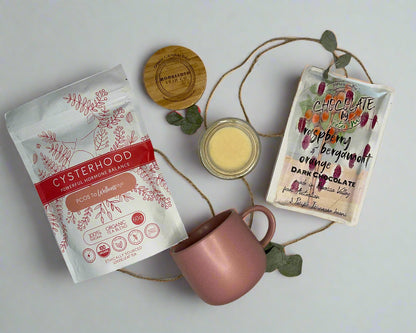 Pink mug, packets of tea, and a small jar on a white surface with decorative elements.