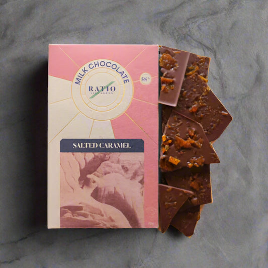 Milk chocolate bar with salted caramel pieces next to its packaging on a white background