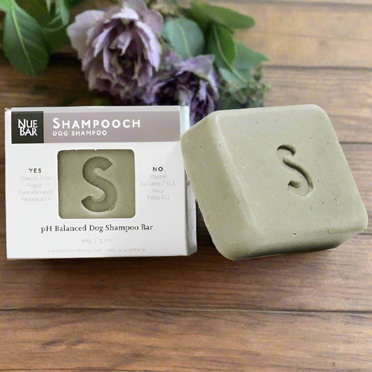 A packaged dog shampoo bar labeled 'NueBar Shampooch pH Balanced Dog Shampoo Bar' next to its unscented gray bar.