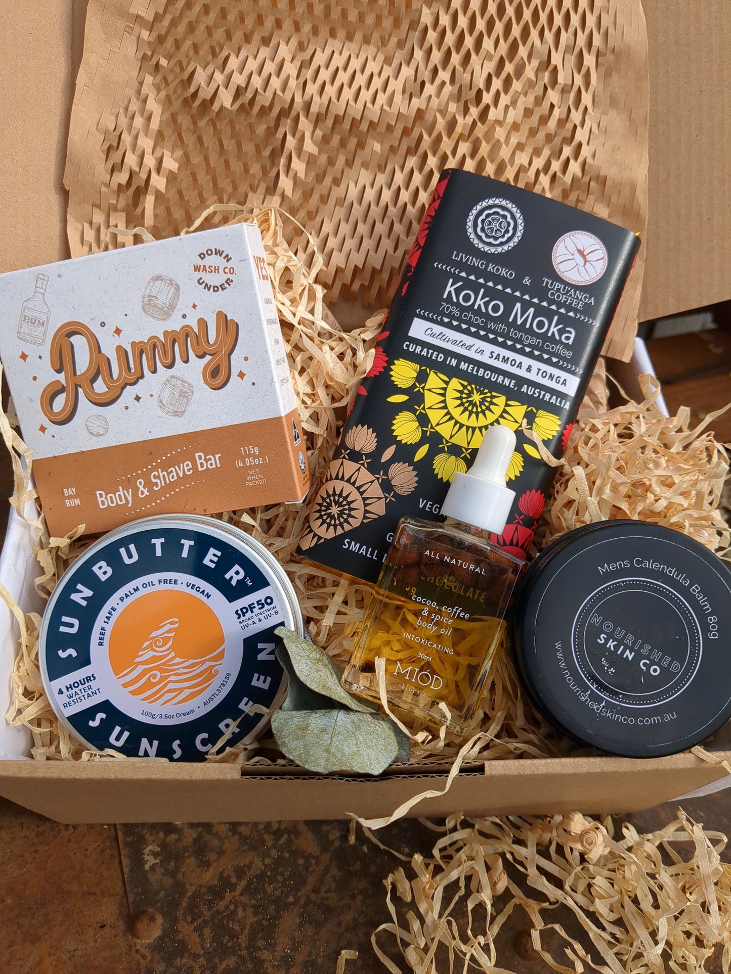 Assorted products including a box labeled 'Koko Hola', a bottle, and a jar in a box with straw-like material.