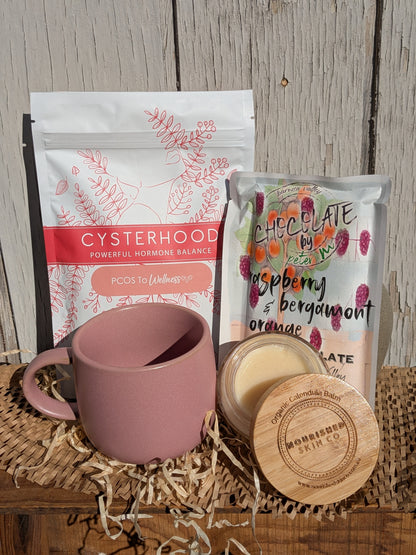 Pink mug with a package of 'Cysterhood' and a chocolate bar on a wooden surface.
