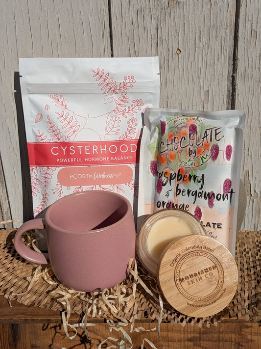 Pink mug with a package of 'Cysterhood' and a chocolate bar on a wooden surface.